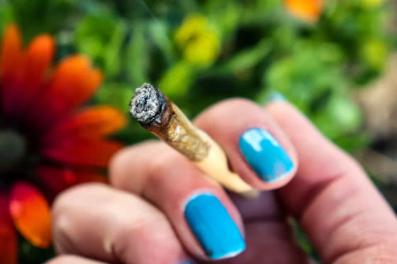 woman holding burning joint of weed with ash